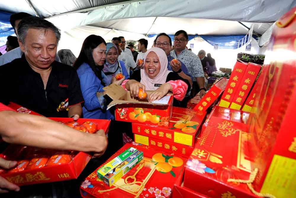 Lilis Saslinda (kanan) mengagihkan buah limau kepada pengunjung sempena Jualan Rahmah Tahun Baharu Cina di Block 56 flat Taman Ungku Tun Aminah, Johor Bahru pada Sabtu.