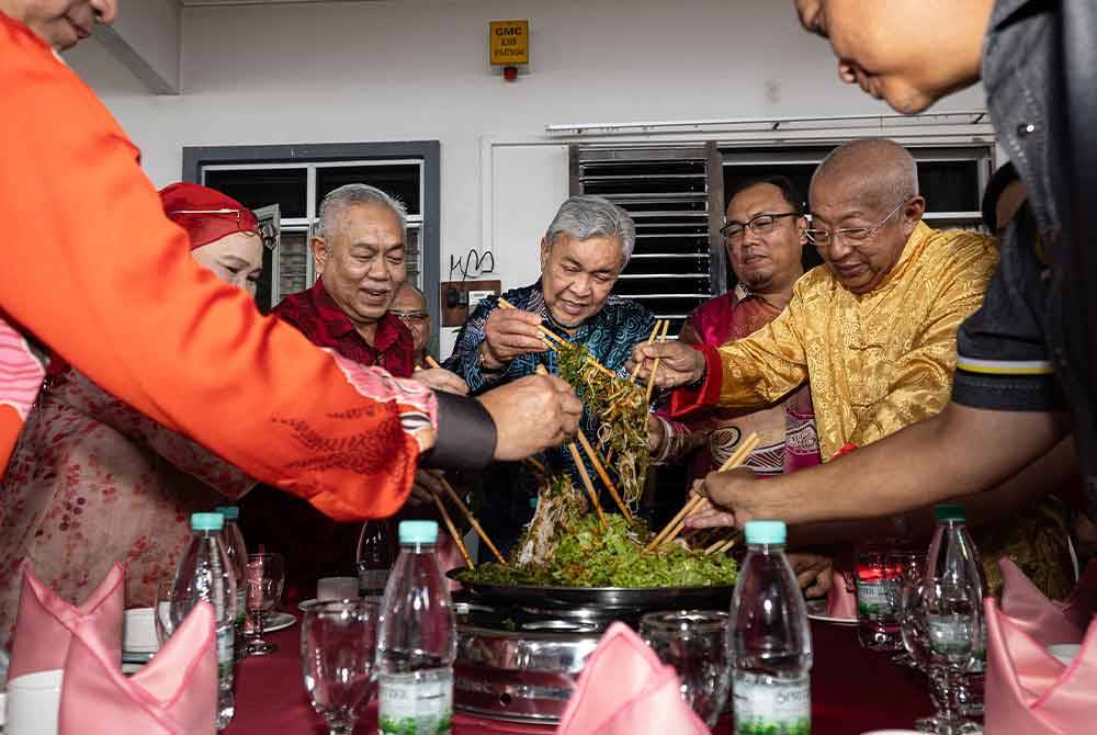 Ahmad Zahid menggaul Yee Sang bersama keluarga angkatnya pada Majlis Kunjungan Kasih Tahun Baharu Cina di Taman Desa Bersatu Simpang Empat, Hutan Melintang, hari ini. Foto Bernama