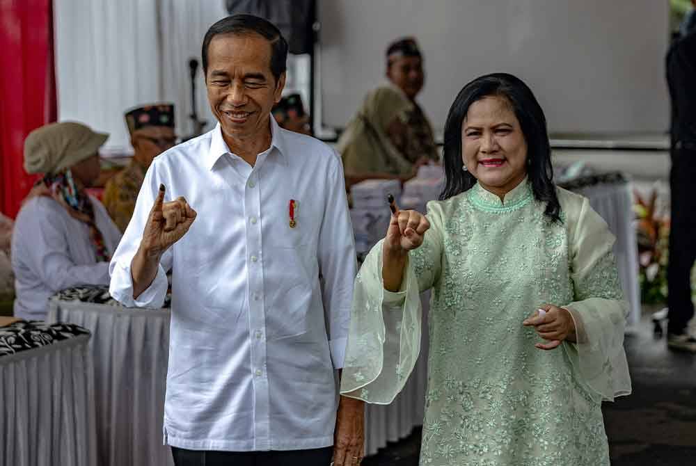 Jokowi diiringi Wanita Pertama, Iriana menunjukkan jari dicelup dakwat selepas membuang undi di Jakarta.