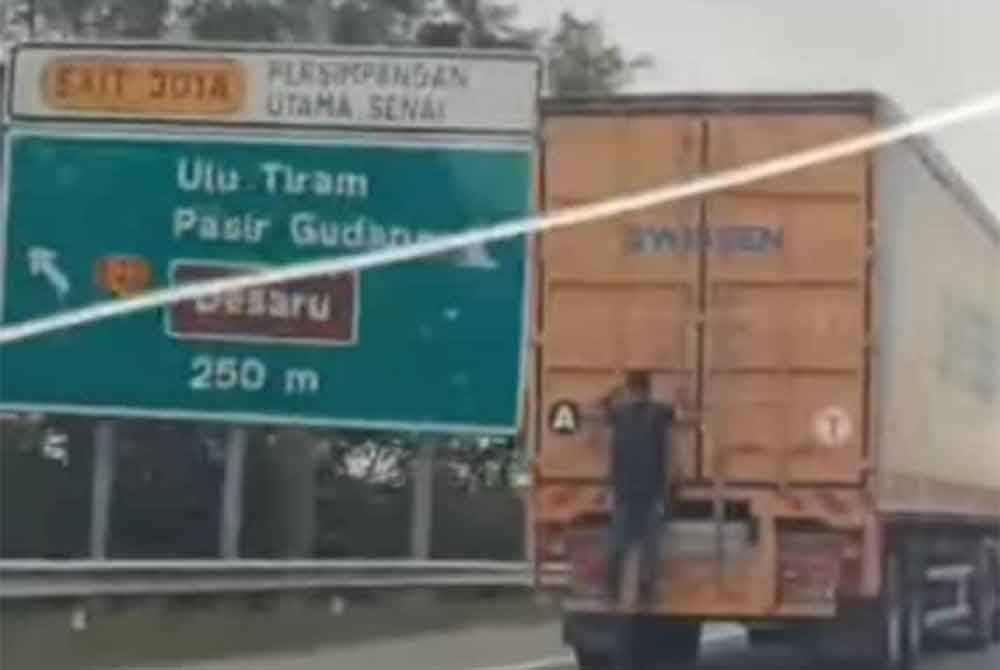 Tangkap layar memaparkan seorang lelaki berpaut sedang di belakang sebuah treler sedang bergerak di Lebuhraya Link Kedua, Kulai, pada Khamis