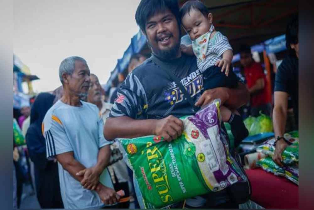 Pengunjung membawa barang keperluan yang dibeli dengan harga murah berbanding harga asal sempena Program Jualan Agro Madani di Pasar Tani Merlimau hari ini. Foto Bernama