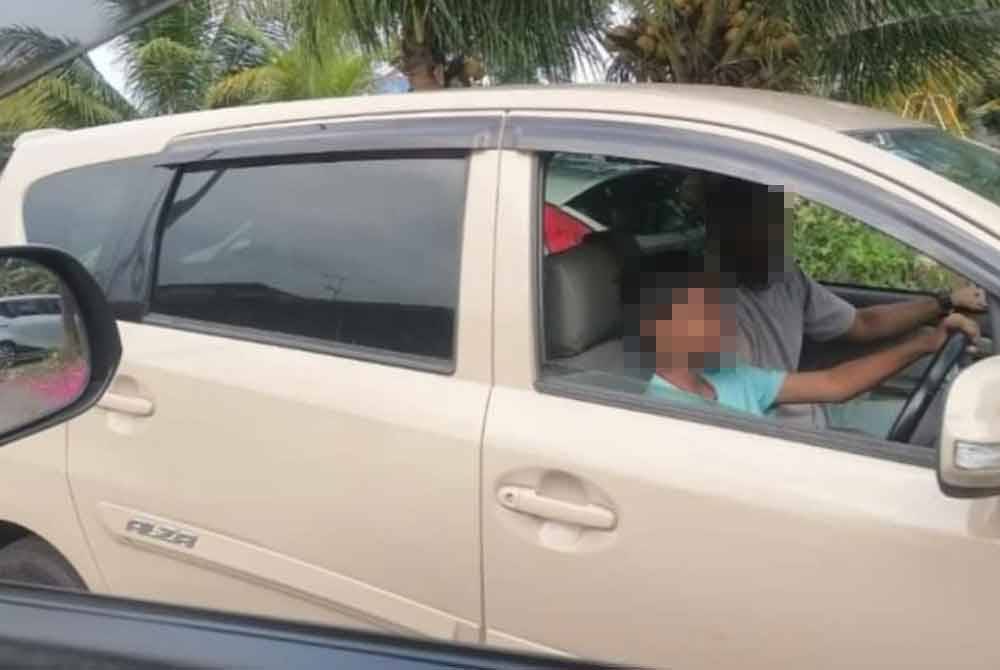 Tangkap layar paparan kanak-kanak memandu kereta di jalan raya awam dengan seorang lelaki dewasa duduk di sebelah tempat penumpang.