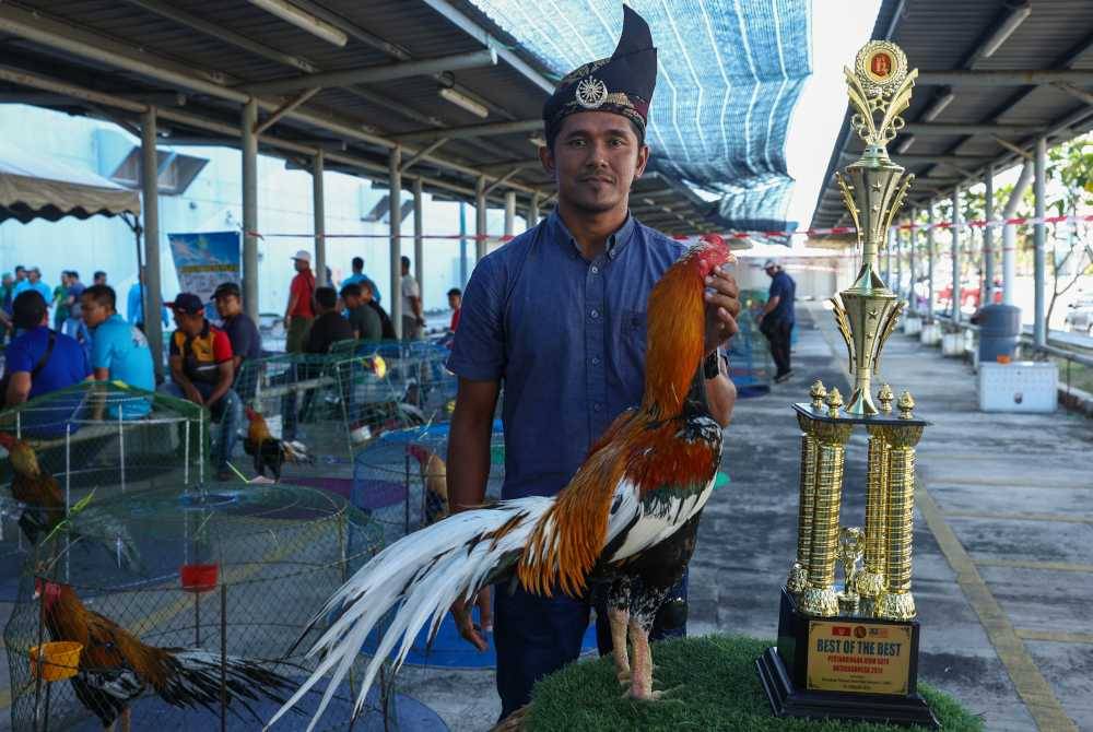 Pemilik Ayam Ratu, Roshairi Izwan Sulaiman bersama ayam baka Leung Hang Khao (LHK) yang diberi nama Mongkut bergambar bersama piala yang dimenanginya dalam Pertandingan Ayam Ratu Peringkat Nasional anjuran Persatuan Peminat Ayam Ratu Kelantan (PARK) di Pusat Beli-belah AEON Mall Kota Bharu hari ini. Foto Bernama