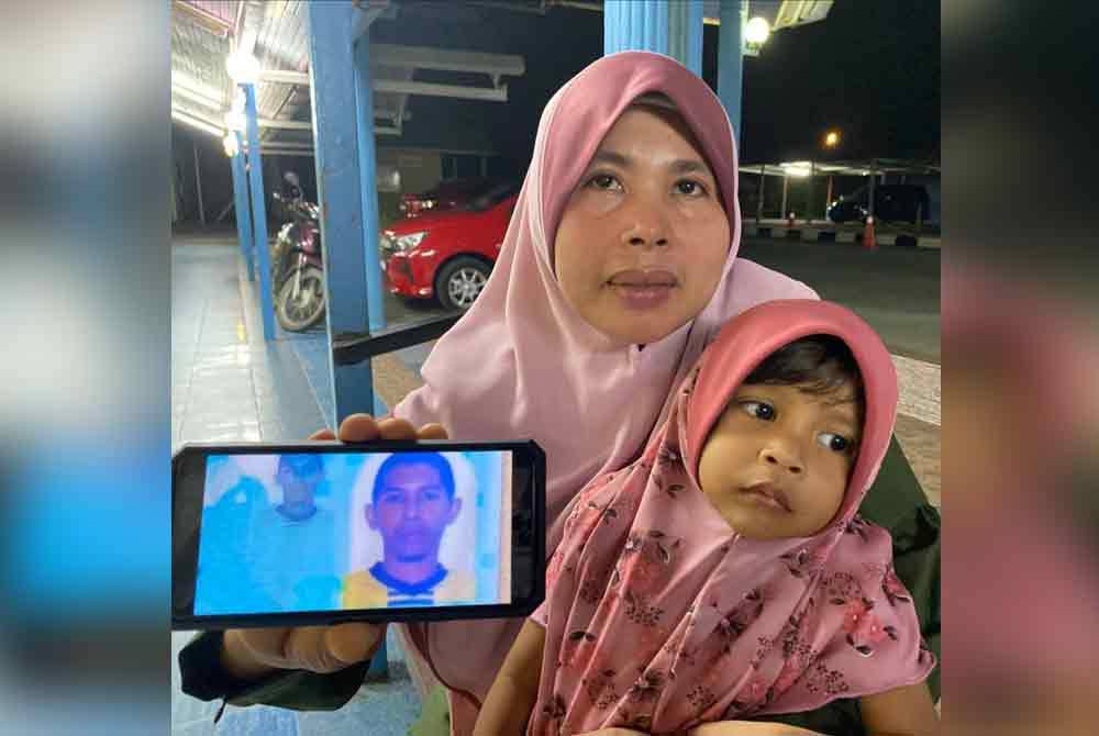 Rohaya memangku anak bongsunya sambil menunjukkan gambar arwah suami ketika ditemui di Unit Perubatan Forensik Hospital Pasir Mas.