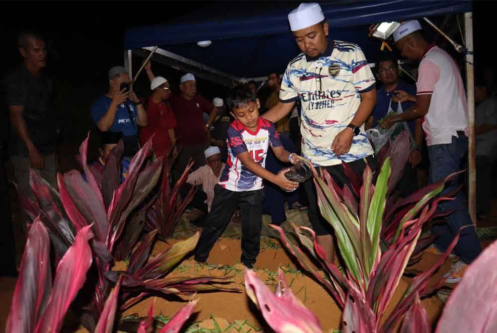 Attar Azim (kiri) ditemani bapa saudara menyiram air di atas kuburan ahli keluarganya.