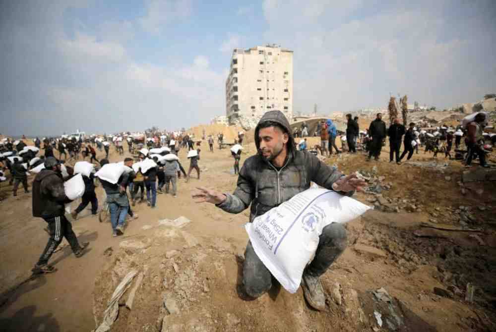 Pelarian Palestin membawa guni tepung dari trak bekalan bantuan kemanusiaan dekat pos kawalan Israel di Gaza. Foto Agensi