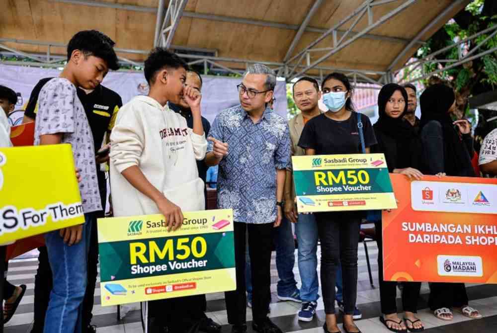 Fahmi Fadzil (tiga dari kiri) beramah mesra bersama para penerima sumbangan Kembali ke Sekolah pada Program ‘Back To School’ Bersama Suruhanjaya Komunikasi dan Multimedia Malaysia (MCMC) dan Shopee di PPR Sri Pantai, hari ini. Foto Bernama