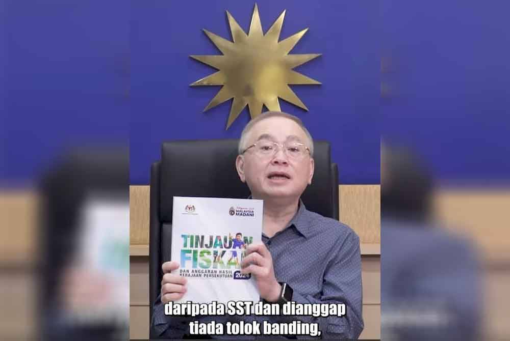 Ka Siong menunjukkan buku Tinjauan Fiskal 2024 yang menyenaraikan perbandingan sistem percukaian GST dan SST.