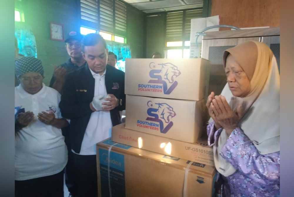 Onn Hafiz (kiri) menyerahkan sumbangan kepada Rahmah (kanan) di Kampung Sungai Kuali, Serkat di Pontian pada Ahad.