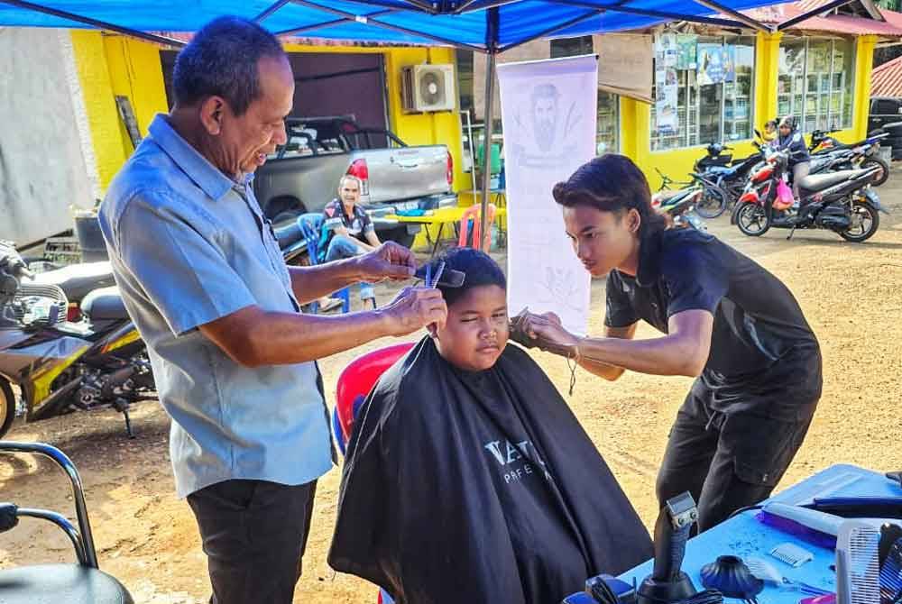 Razak (kiri) membantu menggunting rambut seorang peserta sempena program gunting rambut percuma di Jengka.