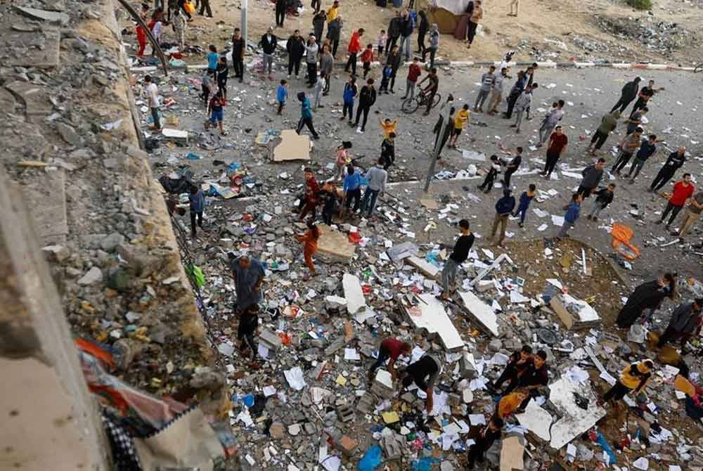 Orang ramai berjalan di antara serpihan di tapak serangan Israel ke atas bangunan pangsapuri di tengah-tengah konflik berterusan antara Israel dan kumpulan Palestin Hamas di Khan Younis di selatan Semenanjung Gaza - Foto: Reuters