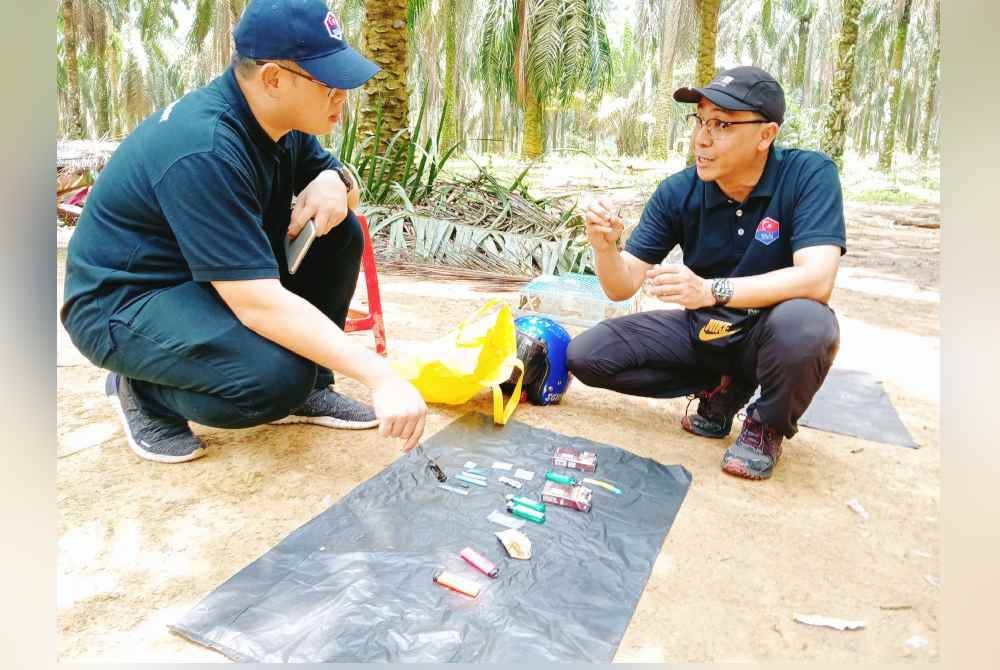 Tian Soon (kiri) dan Azli melihat barang milik penagih selepas melakukan serbuan di sebuah ladang kelapa sawit berhampiran Bukit Dahlia, di Pasir Gudang pada Ahad.