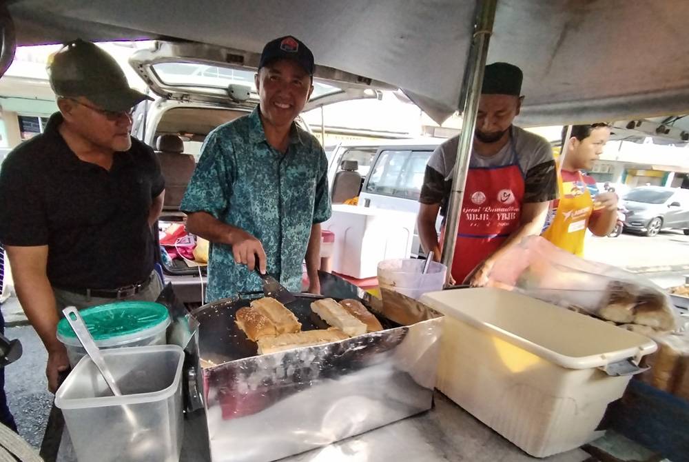 Mohd Jafni (tengah) memasak roti John ketika melakukan lawatan ke tapak bazar Ramadan Bandar Baru UDA, pada Selasa.