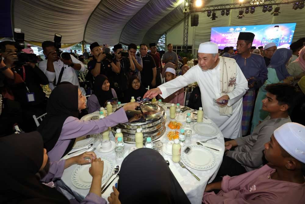 Ahmad Zahid (berdiri dua, kanan) menyampaikan sumbangan duit raya kepada anak-anak yatim yang hadir pada Majlis Santunan Kasih Ramadan di pekarangan Masjid Jamek Pekan Layang-Layang, Simpang Renggam pada Khamis. Foto Bernama