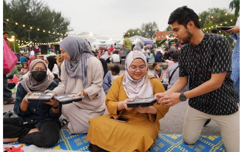 Pengurus Besar Strategi Korporat PHB, Muhammad Zikri Kamardin (kanan) bersama kakitangan PHB mengedarkan bungkusan menu berbuka puasa kepada orang ramai yang hadir pada program Iftar Ala Madinah@Karangkraf pada Jumaat.