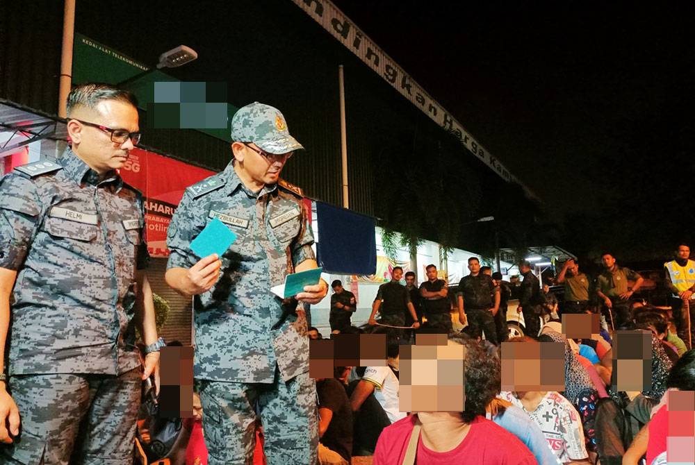 Meor Hezbullah (dua dari kiri) memeriksa dokumen perjalanan milik seorang warga asing dalam serbuan di Rumah Pangsa Bercham dekat Ipoh pada Sabtu.