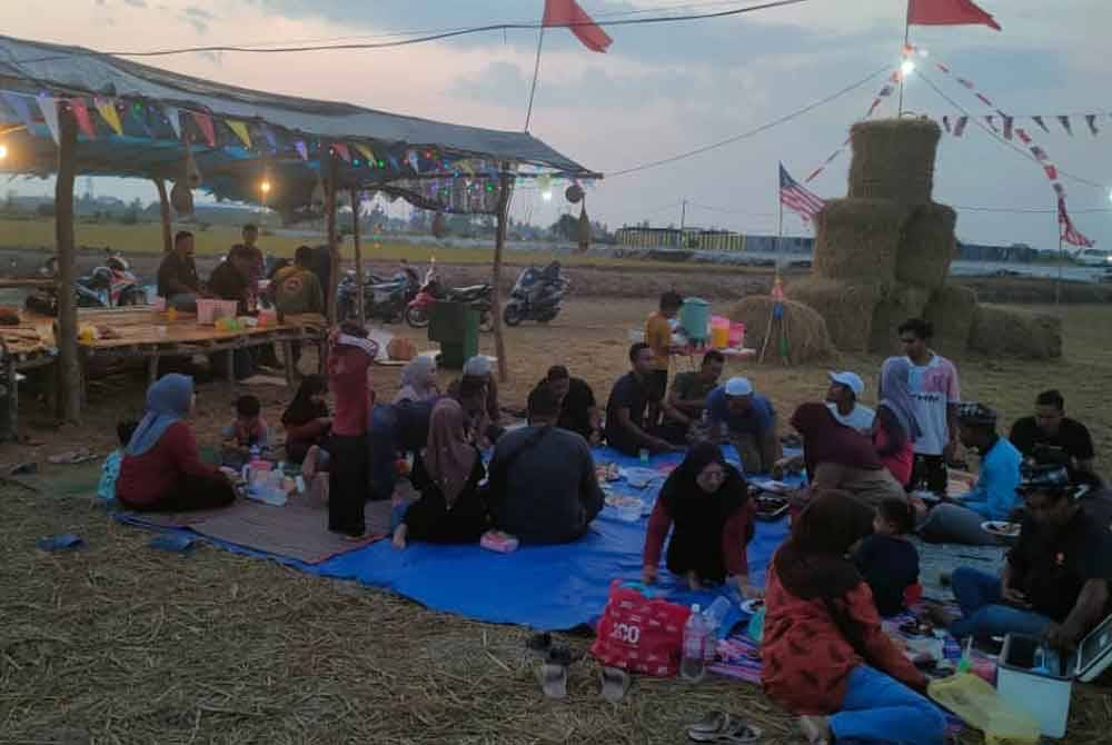 Penduduk berbuka puasa sambil menikmati panorama replika jerami gulung di Kampung Kelompang.