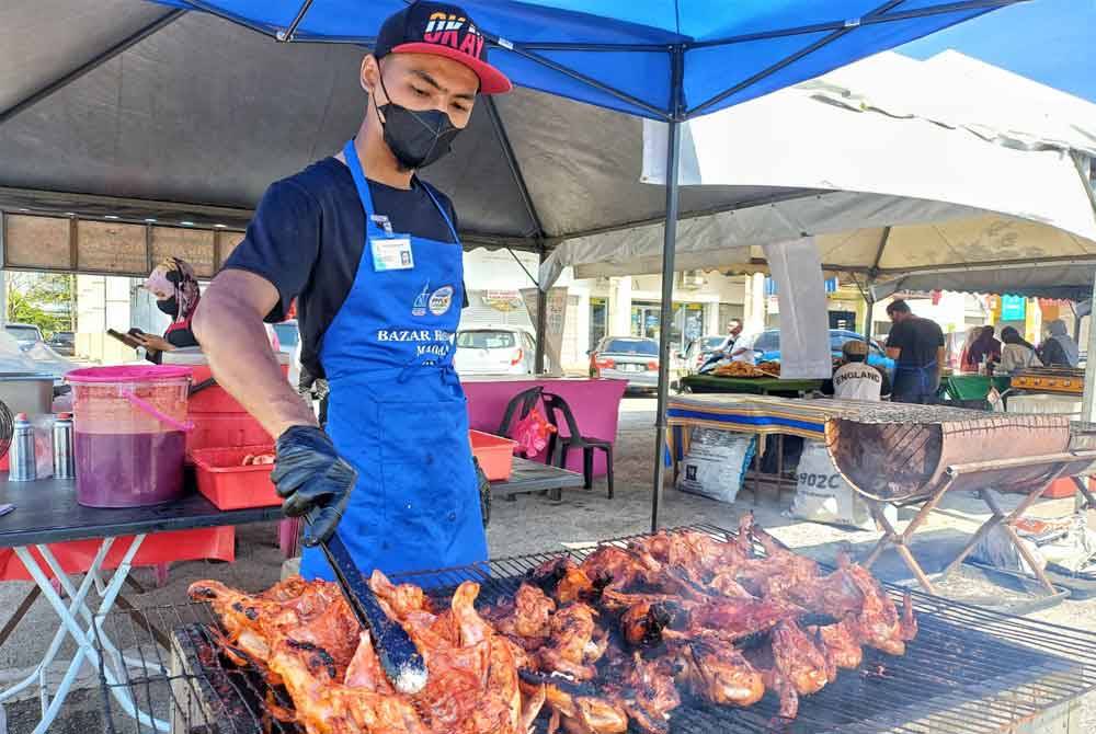 Pekerja kepada Siti Sarah memasak ayam bakar berempah di bazar Ramadan Sungai Isap pada Sabtu