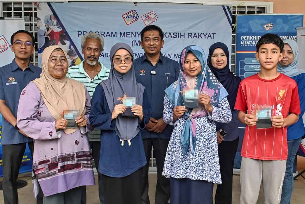 Ketua Pengarah Pendaftaran Negara Badrul Hisham Alias (tengah) bergambar bersama penerima kad pengenalan baharu yang merupakan mangsa banjir pada Program Menyemai Kasih Rakyat (Mekar) JPN di Kampung Pasir Raja pada Sabtu. Foto Bernama