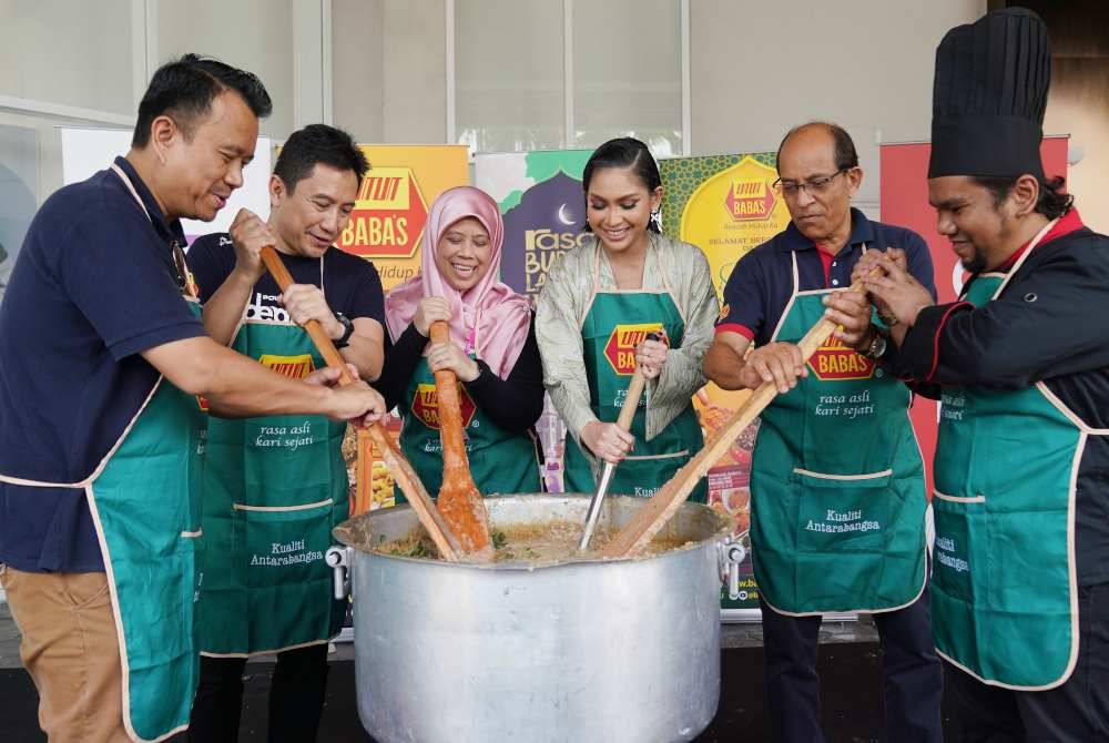 Azrain (kiri), Syamil (dua dari kiri) dan Sissy Iman (tengah) menggaul bubur lambuk percuma buat pengunjung pasar raya AEON, para petugas dan komuniti setempat di pasar raya AEON pada Sabtu.
