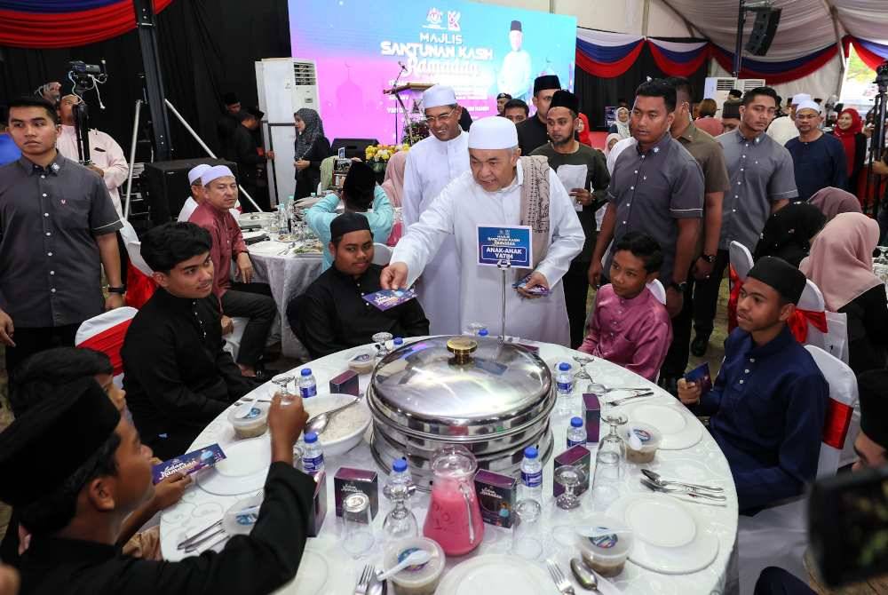 Ahmad Zahid (tengah) menyampaikan sumbangan duit raya kepada anak-anak yatim terpilih pada Majlis Santunan Kasih Ramadan bersama Kementerian Kemajuan Desa dan Wilayah 2024 di Masjid Sultan Mahmud Bandar Al Muktafi Billah Shah. Foto Bernama