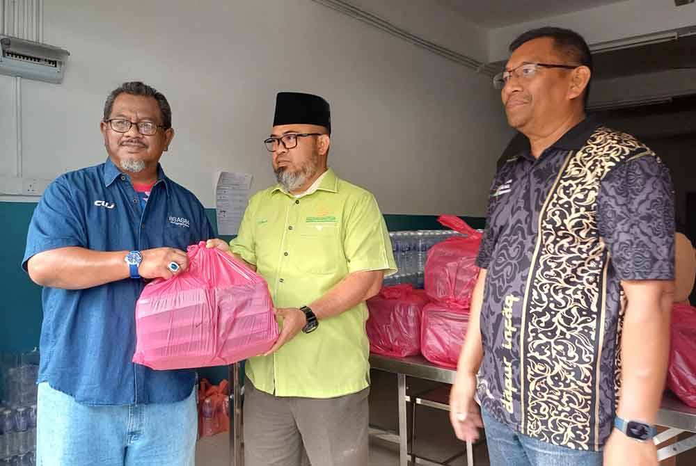 Asmadi (tengah) memberi bungkus makanan kepada wakil NGO sambil ditemani Badrul Jamili di Pusat Prihatin Pahang, Jalan Wong Ah Jang.