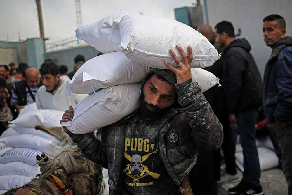 Seorang lelaki Palestin membawa guni bantuan kemanusian UNRWA di pusat pengedaran di Rafah. - Foto: AFP