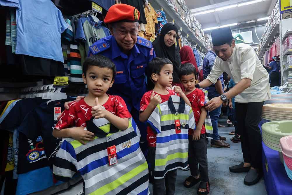 Mohd Azlan (kanan) mencuba memadankan pakaian kepada penerima sempena Program Meriah Beraya Sejahtera Bersama di Pasar Raya Mydin, Pusat Transformasi Luar Bandar (RTC) Perak di Gopeng pada Ahad.