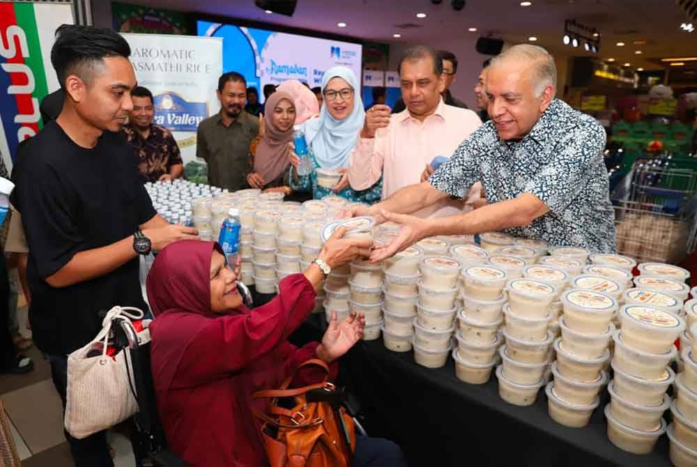 Ameer (kanan) mengedar bubur lambuk kepada pelanggan Mydin USJ pada Sabtu.