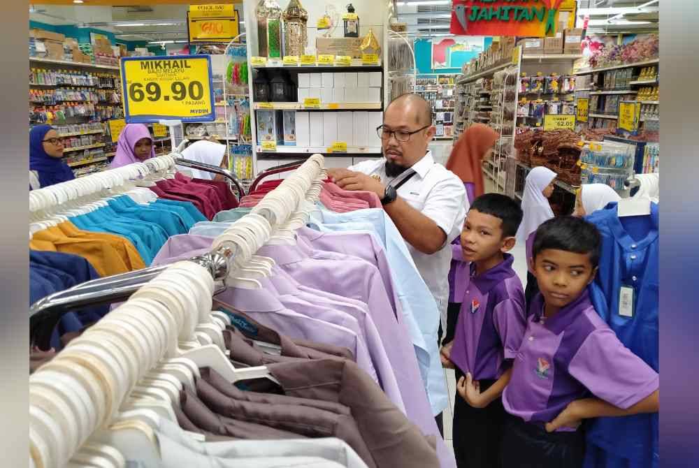 Murid-murid SK Jati memilih pakaian hari raya sumbangan DPMP sambil dibantu guru mereka di Pasar raya Besar Mydin Meru di sini pada Isnin.