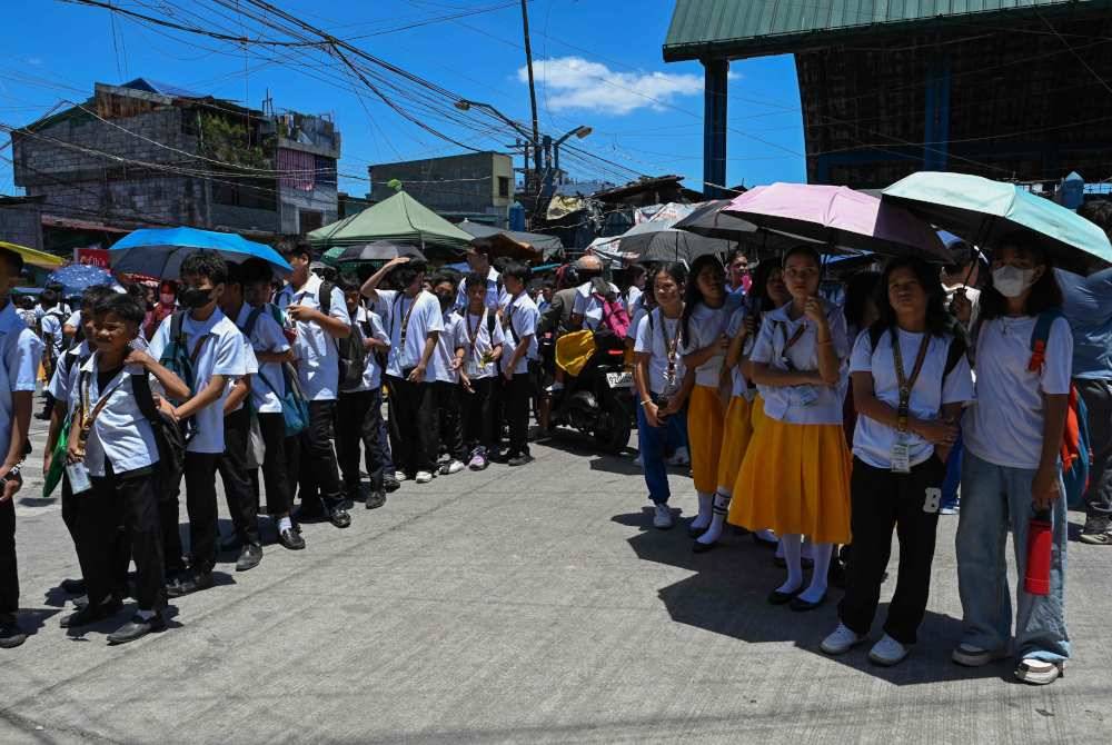 Sebahagian pelajar menggunakan payung bagi melindungi diri mereka daripada bahang panas matahari ketika beratur di luar sekolah mereka di Manila pada Selasa. Foto AFP