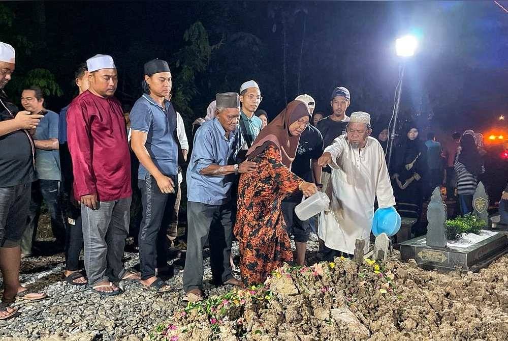 Kakak Allahyarham, Teh Awang (tengah) menyiram air di pusara Allahyarham Jaafar Onn di Tanah Perkuburan Islam Al Firdaus Tanjung Gading, Muar pada malam Rabu.