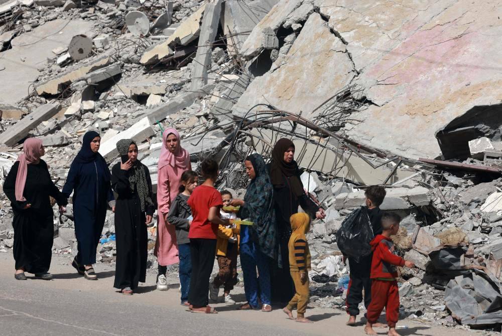 Wanita dan kanak-kanak Palestin berjalan berhampiran bangunan yang musnah akibat serangan bom Israel di Rafah, selatan Semenanjung Gaza pada Ahad, di tengah-tengah konflik berterusan antara Israel dan pejuang Hamas. Foto AFP