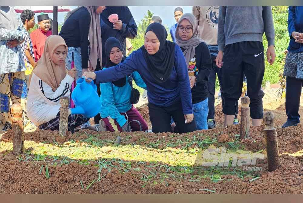 Norzalifa menyiram pusara kedua anaknya yang dikebumikan dalam satu liang lahad di Tanah Wakaf Perkuburan Islam Kampung Perik, Enggor.