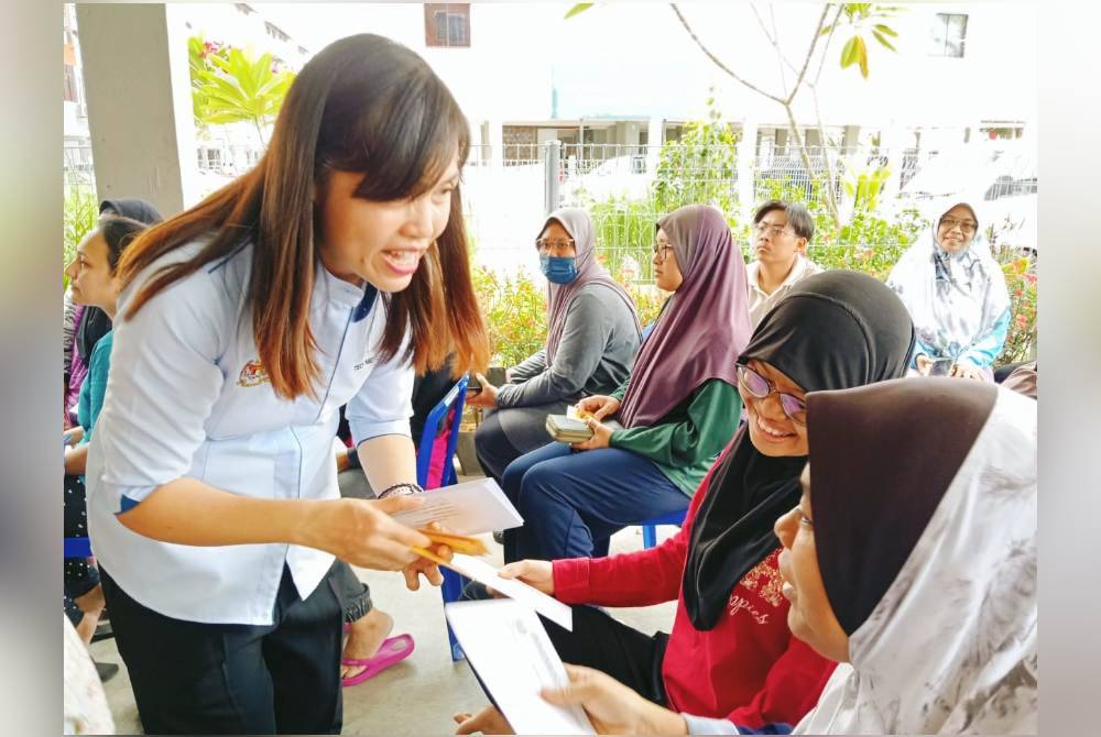 Nie Ching (kiri) menyampaikan sumbangan duit raya kepada penerima dalam Program Projek Baju Raya Terpakai dan Sumbangan Bantuan Raya di Blok 3 Flat Taman Putri, Kulai pada Sabtu