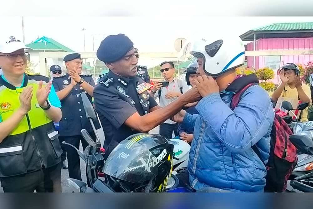 M Kumar memakaikan topi keledar kepada penunggang motorsikal pada Program Advokasi Polis Diraja Malaysia (PDRM) bersama Pertubuhan Keselamatan Sosial (PERKESO) sempena Ops Selamat 22/2024 Aidilfitri di Plaza Tol Kempas pada Sabtu.