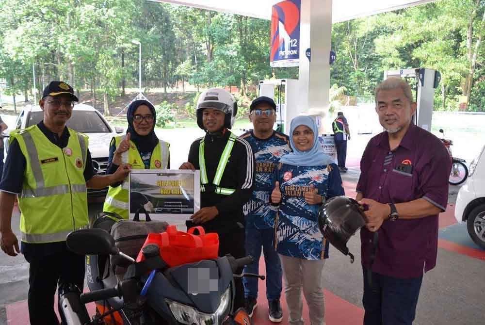 Rahilah (dua dari kanan) bersama Hashim (kanan) menukar topi keledar baharuseorang penunggang motosikal yang mengisi minyak di Petron.