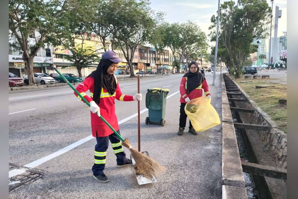 Zawiyah (kiri) dan Siti Khatijah melakukan tugas menyapu sampah di tepi jalan utama di tengah bandaraya Kuantan.