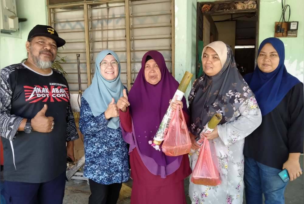 Borhan (kiri) dan Fadziah (kanan) menyerahkan lemang serta rendang kepada penerima di Taman Perpaduan, Ipoh pada Khamis.