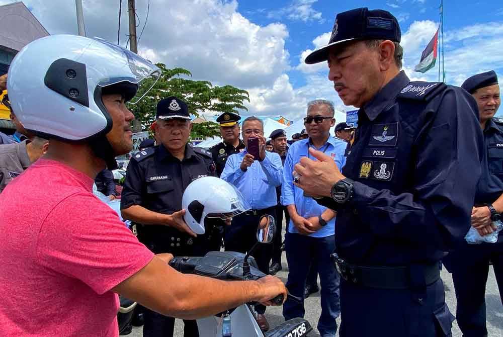 Muhamad Zaki (kanan) menyampaikan topi keledar kepada pengguna jalan raya semasa Program Keselamatan Jalan Raya Ops Selamat 22/2024 Sempena Aidilfitri di hadapan Balai Polis Binjai, di Kota Bharu pada Isnin.