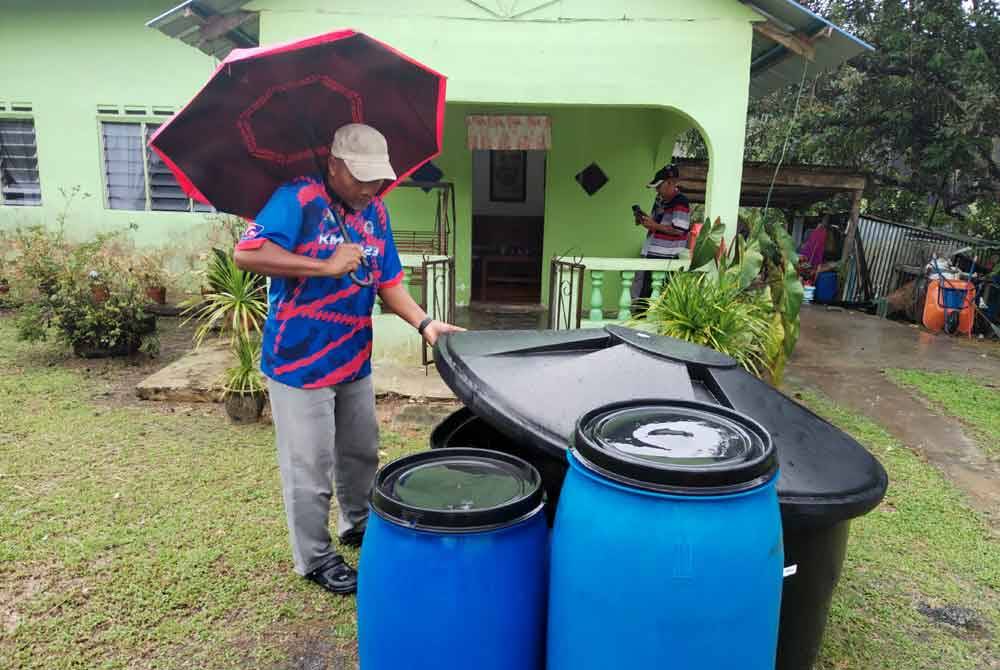 Zaman menunjukkan tiga tong di hadapan rumahnya untuk menadah air.