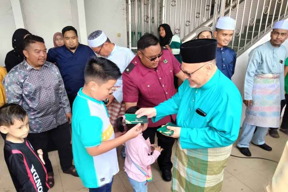 Mohd Amar menyampaikan duit raya kepada kanak-kanak sempena Majlis Rumah Terbuka Aidilfitri Pas Kawasan Pengkalan Chepa pada Sabtu.