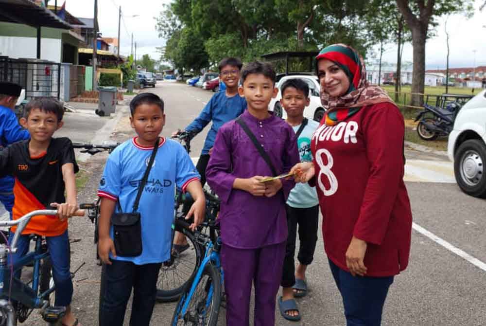 Faridah (kanan) menerima sumbangan duit raya daripada Mohd Rayyan di hadapan rumahnya di Taman Scientex, Pasir Gudang, pada Ahad.