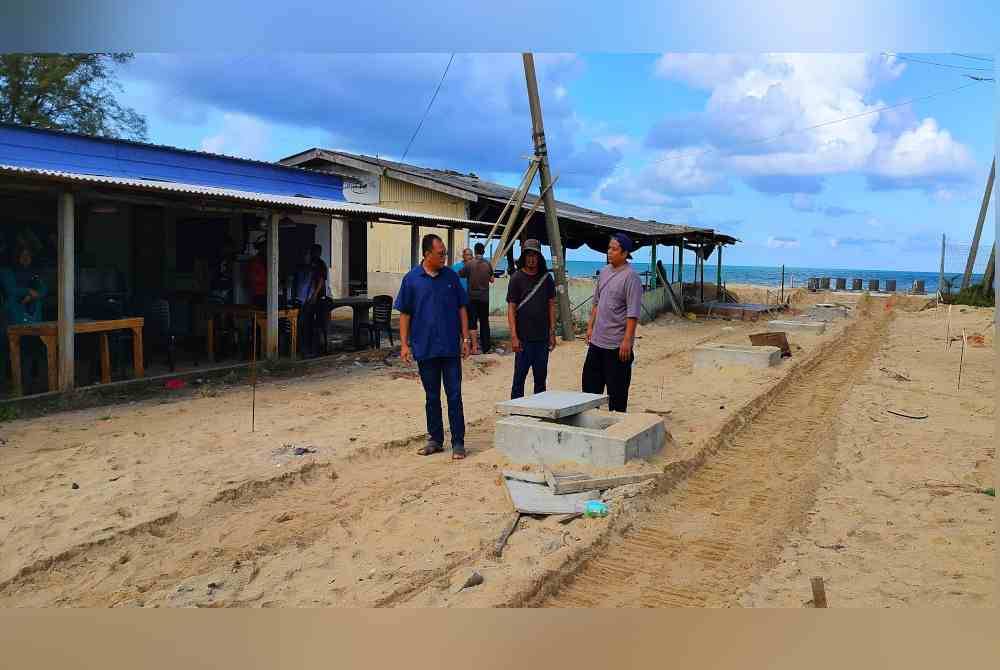 Mohd Fairus (kanan) menunjukkan kepada Andansura (kiri) keadaan longkang mengatasi banjir kilat yang sedang dibina di hadapan kedainya di Pantai Pelindung di sini.