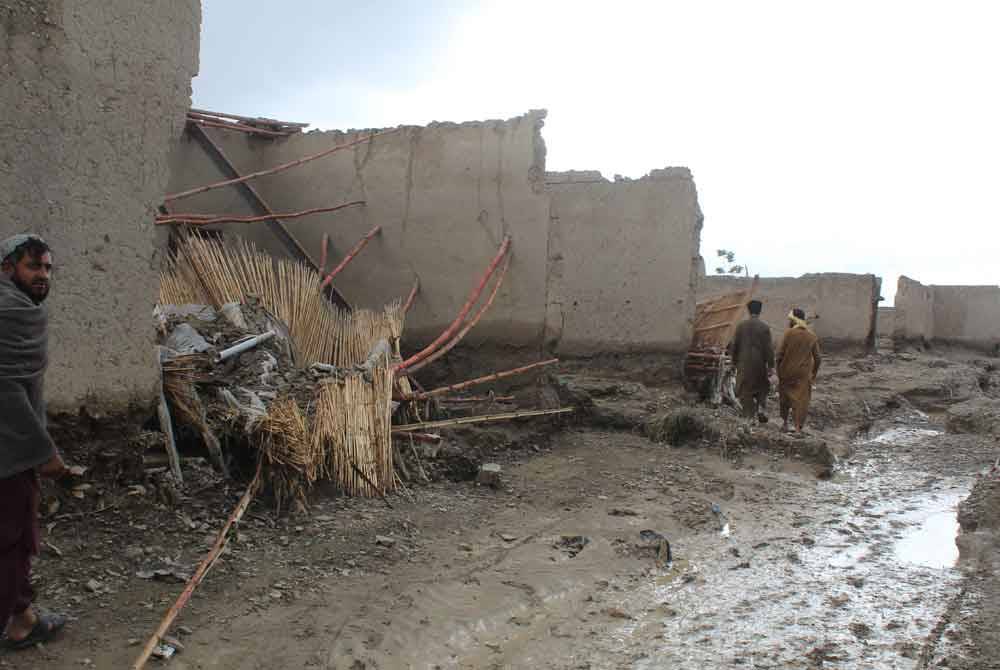 Penduduk berjalan melewati rumah yang musnah akibat hujan lebat di Balochistan, Pakistan, Foto AFP