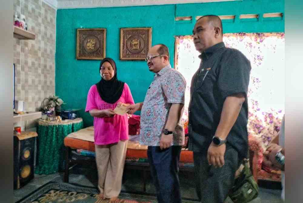 Shamsul Iskandar (tengah) ditemani Zahari (kanan) menyampaikan sumbangan kecemasan Perdana Menteri kepada Fauziah Samat (kiri) di Kampung Bukit Balai, Durian Tunggal di Alor Gajah, pada Isnin.