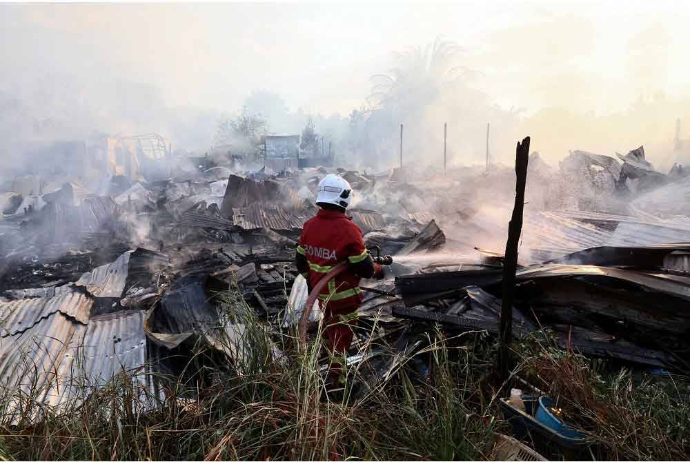 Seorang Anggota Bomba dan Penyelamat memadamkan sisa-sisa api dalam kebakaran rumah di kawasan setinggan di Kampung Magkalinau Parit hari ini. - Foto: Bernama