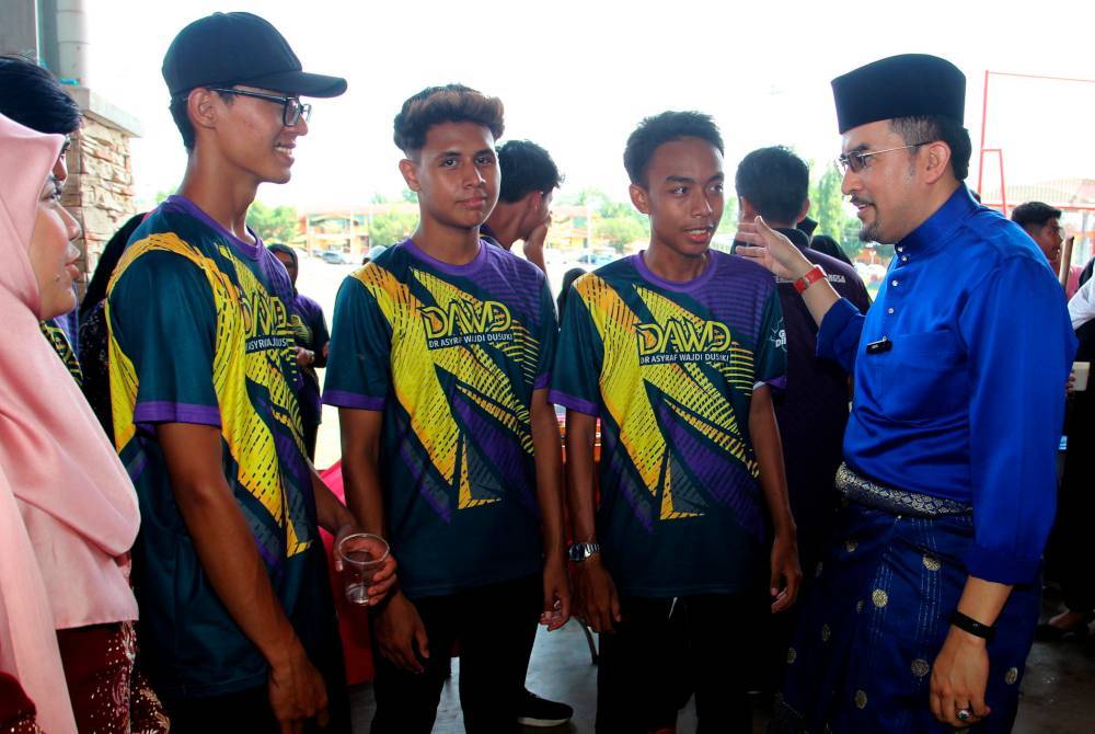 Asyraf Wajdi (kanan) beramah mesra dengan penuntut, Muhammad Irwan Hairudin Hassan (dua dari kanan) ketika hadir pada Hari Mara Bersama Rakyat 2024 dan Rumah Terbuka Aidilfitri Dataran Arena Pengkalan Hulu pada Khamis.