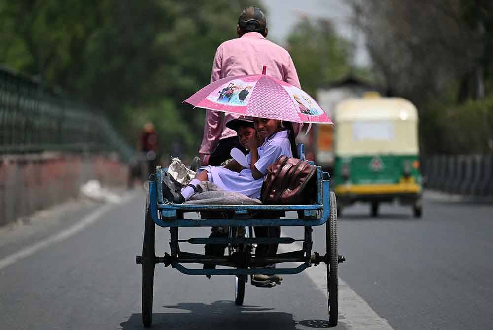 Kanak-kanak berlindung daripada matahari dengan payung semasa melakukan perjalanan di belakang kereta basikal semasa musim panas yang panas di New Delhi pada Khamis. Foto AFP