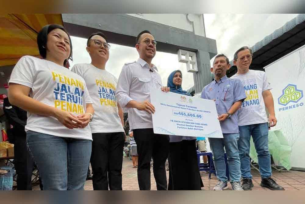 Steven Sim (tiga dari kiri) menyerahkan replika cek tajaan SKSPS untuk penjaja kawasan Bukit Mertajam di Pasar Awam Taman Sri Rambai, Bukit Mertajam pada Sabtu.